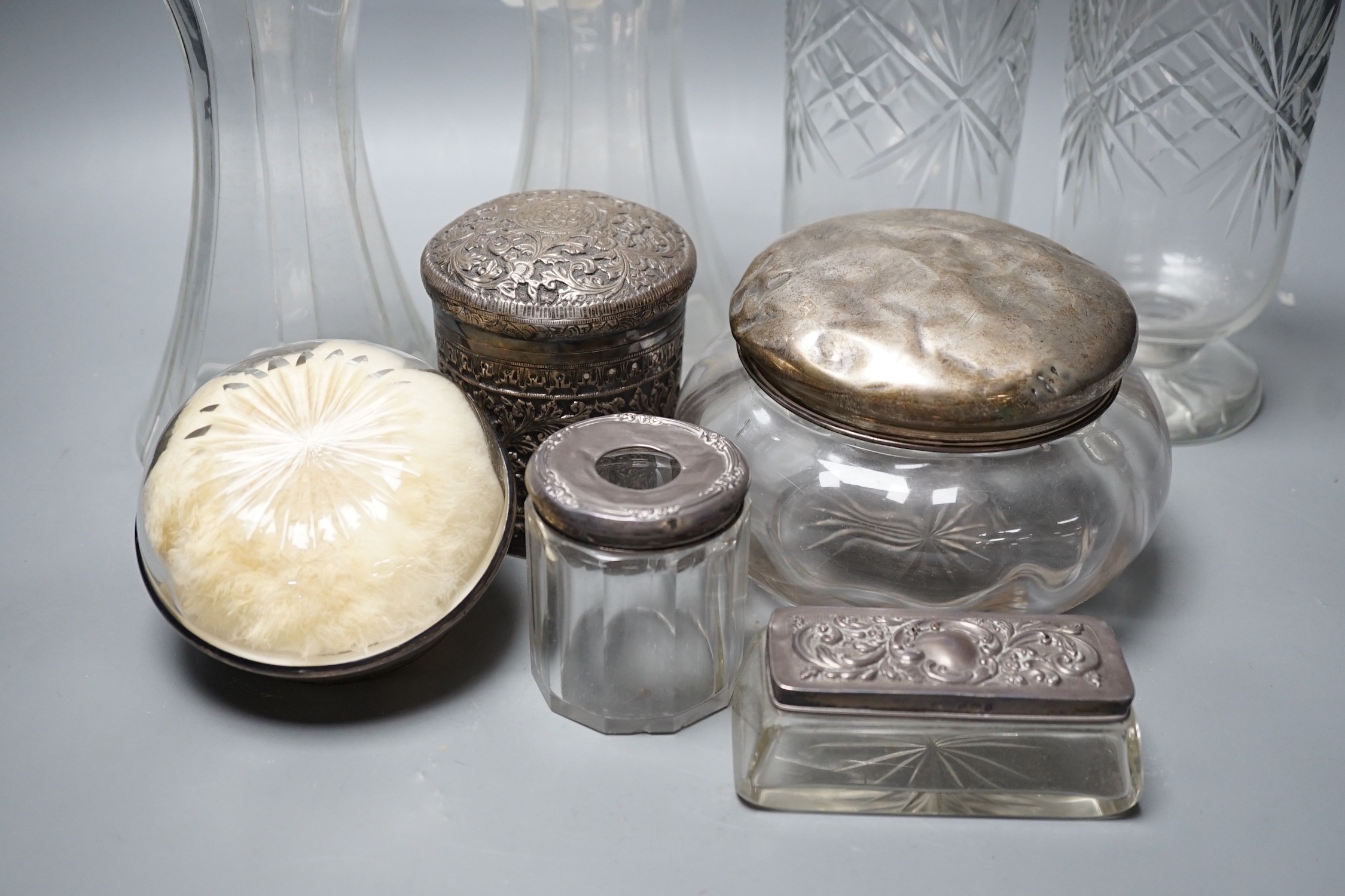 A collection of silver mounted glass items, including a pair of waisted decanters with two silver wine labels, a pair of vases, powder jar etc. and an Indian white metal jar and cover.
